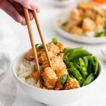 A hand holding chopsticks lifting a piece of Instant Pot orange chicken from a bowl.