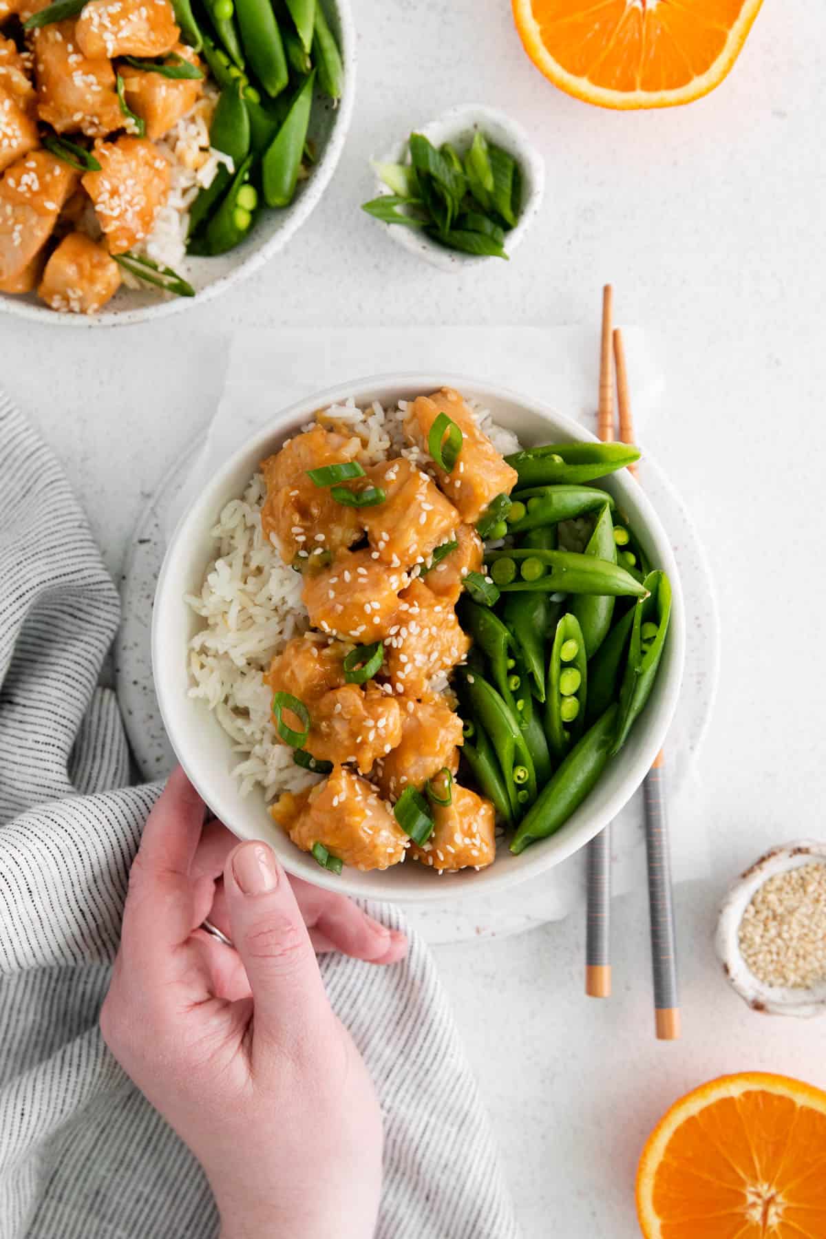 A hand reaching for a bowl of Instant Pot orange chicken.
