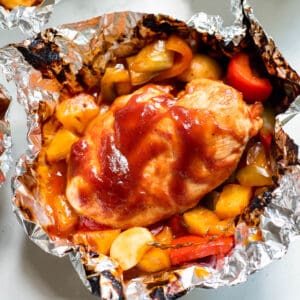 An opened foiled packet with sliced chicken breast, bbq sauce, pineapple and vegetables.