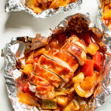 An opened foiled packet with sliced chicken breast, bbq sauce, pineapple and vegetables.