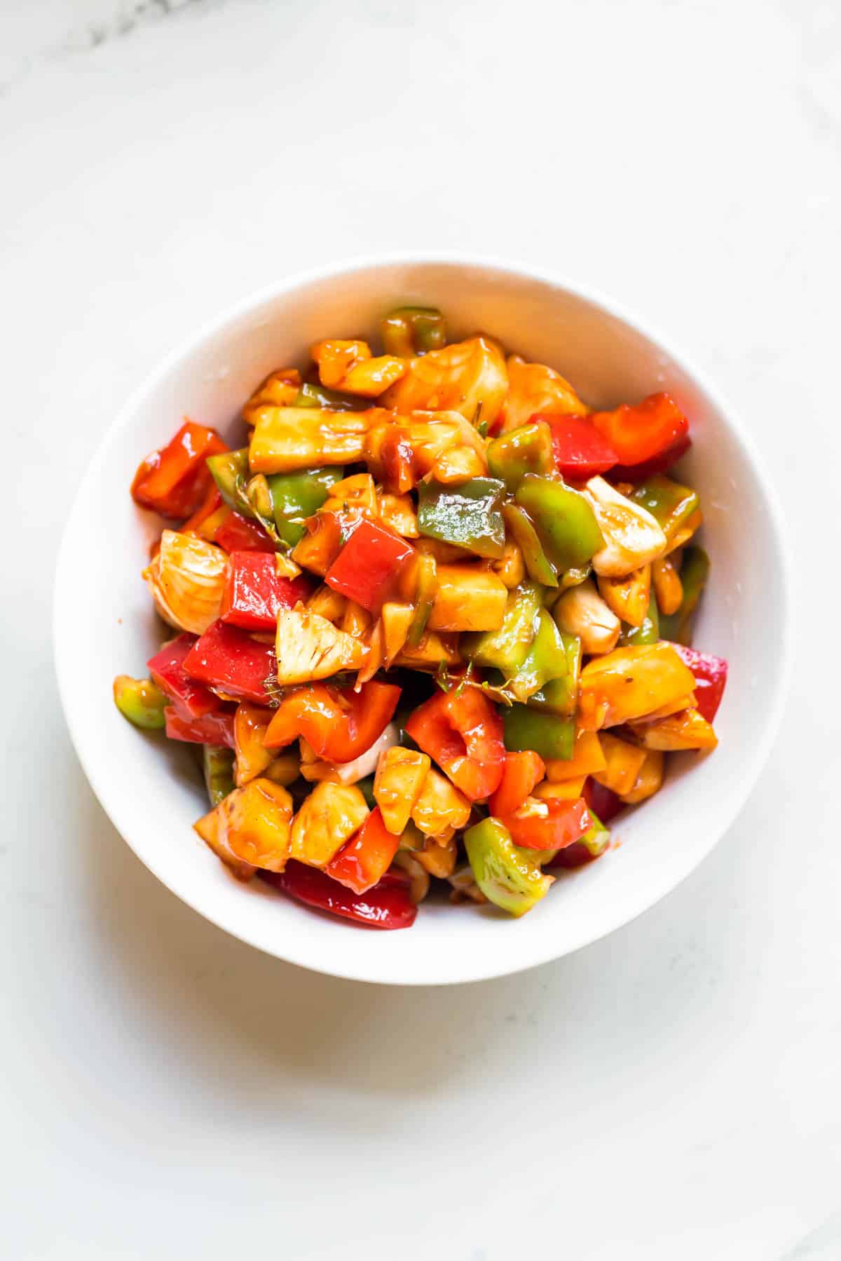 Tossed vegetables and pineapple in sauce in a white bowl.