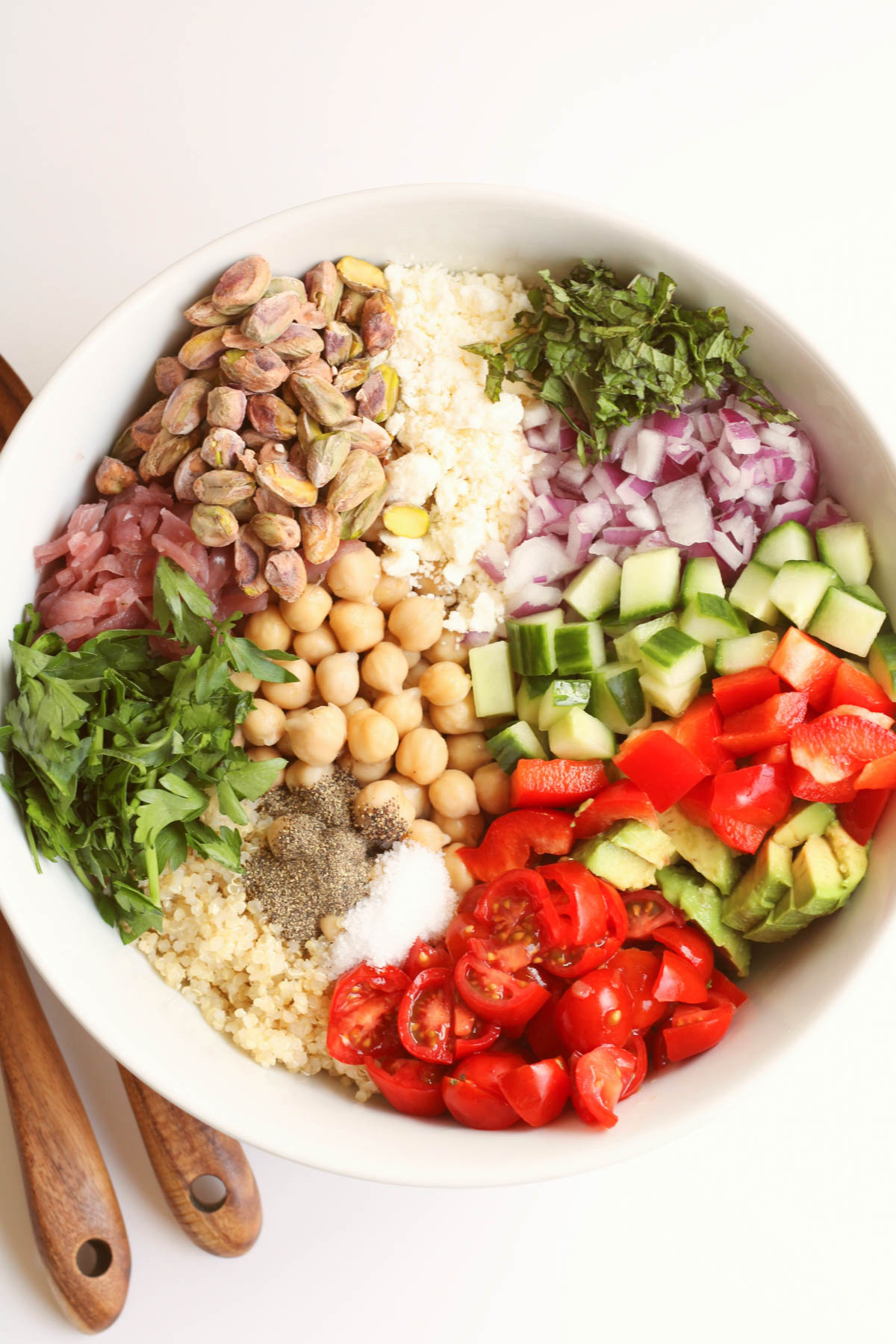 Overhead image of a white bowl containing prepared ingredients for a quinoa salad. 