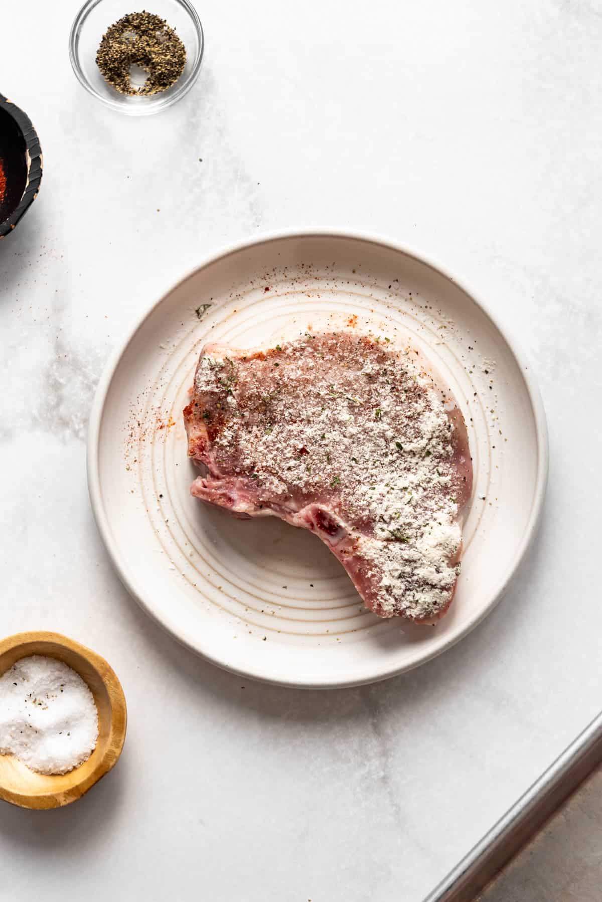 A bone-in pork chop on a plate seasoned with dry powdered ranch dressing mix.