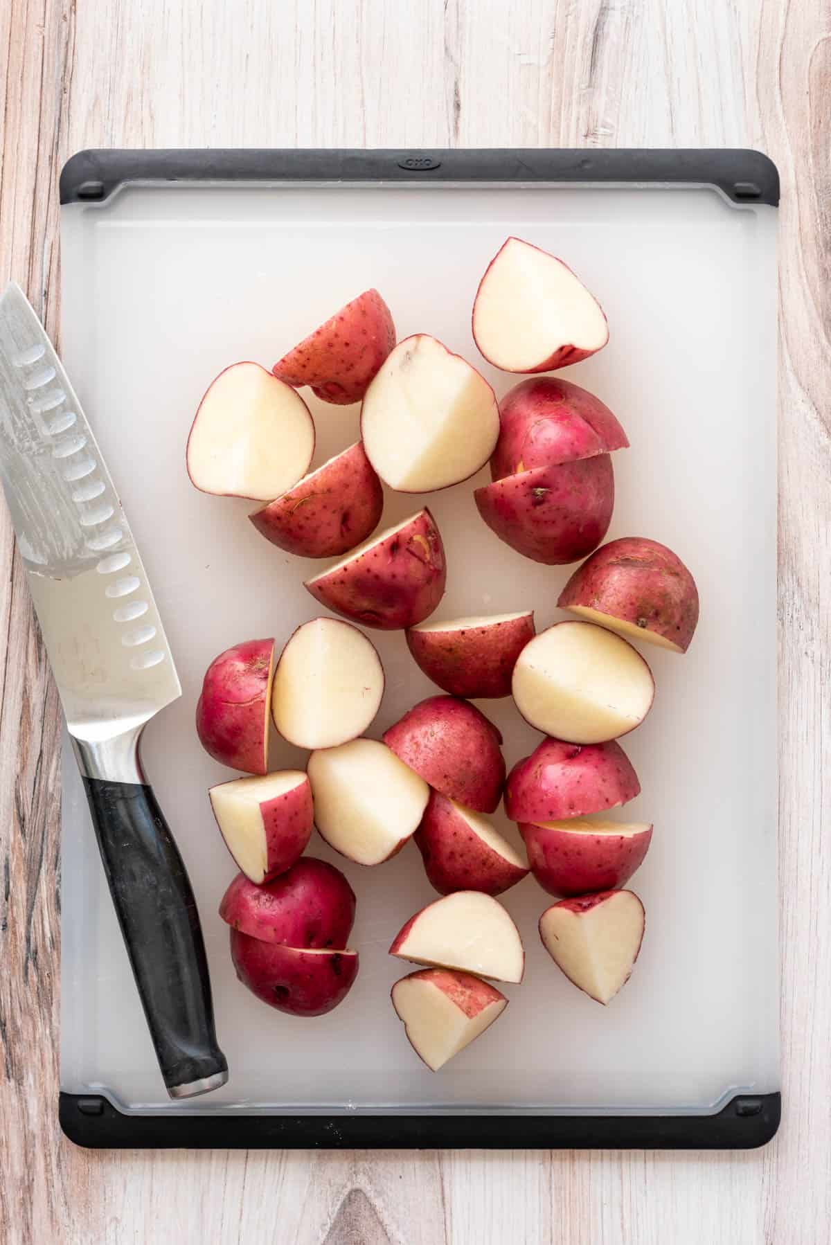 Halved and quartered red potatoes on a cutting board with a knife.