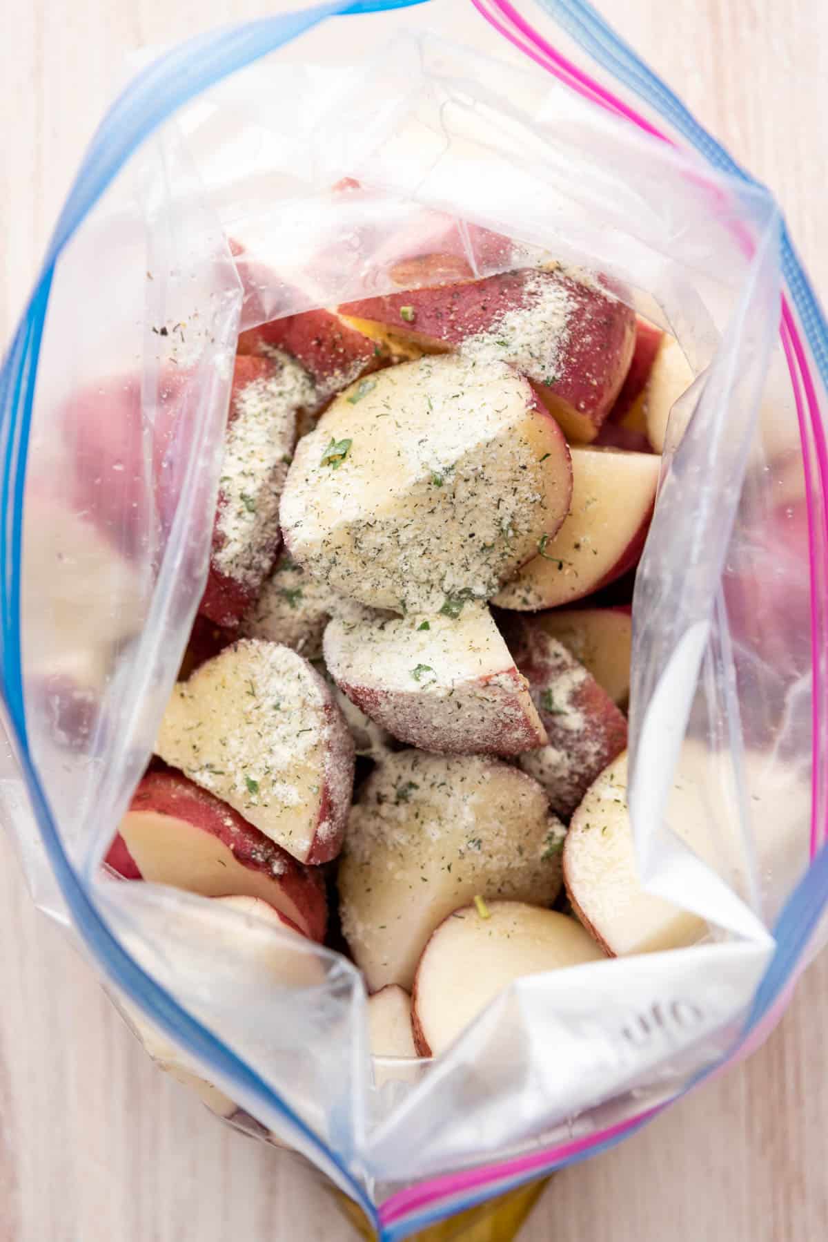 Adding homemade dry ranch seasoning to red potatoes in a Ziploc bag.