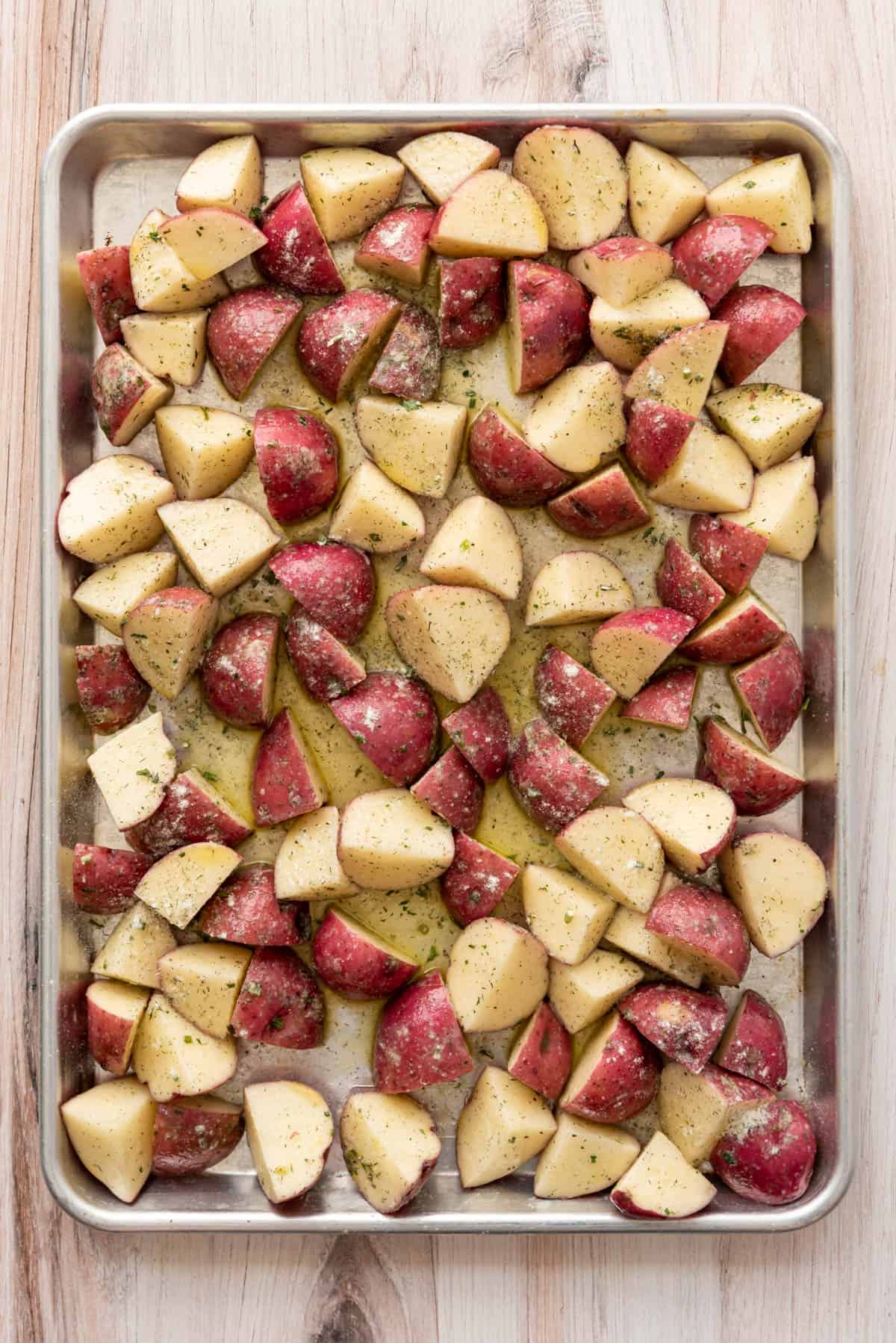 Quartered red potatoes tossed with olive oil and ranch seasoning on a baking sheet.