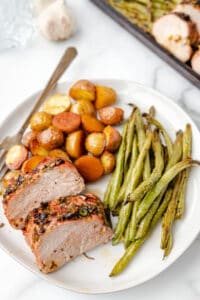 A plate of roasted pork tenderloin with green beans and potatoes.