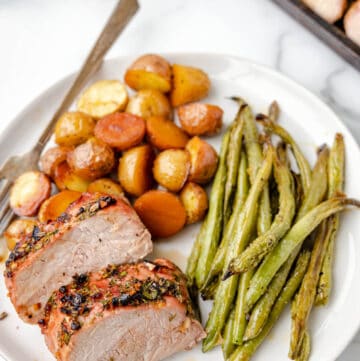 A plate of roasted pork tenderloin with green beans and potatoes.