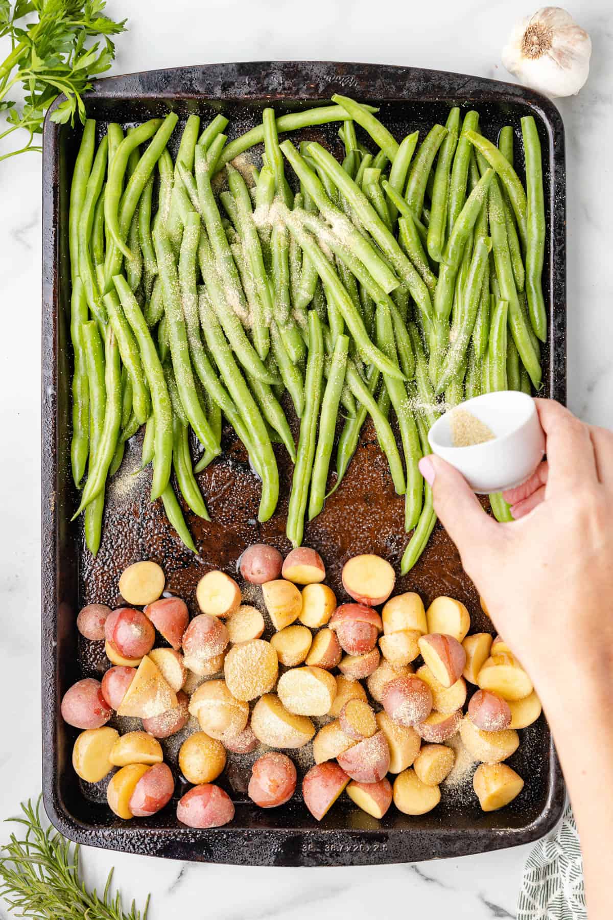 Adding salt to green beans and potatoes on a baking sheet.