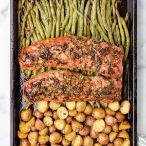 Two whole pork tenderloin roasts on a sheet pan with roasted potatoes and green beans.