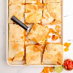 A sheet pan with oven baked quesadillas and a spatula on it.
