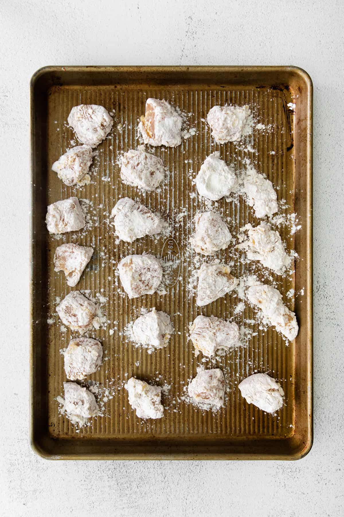 Bite-size chicken pieces arranged in a single layer on a baking sheet.