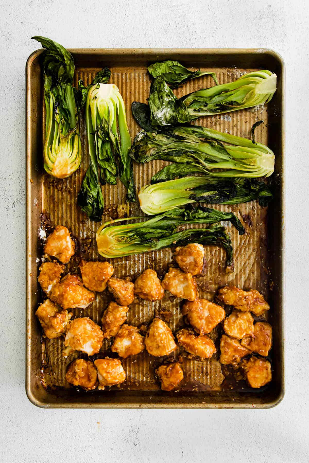Cooked sesame chicken and baby bok choy on a sheet pan.