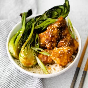 A bowl of baby bok choy with sticky sesame chicken and rice.