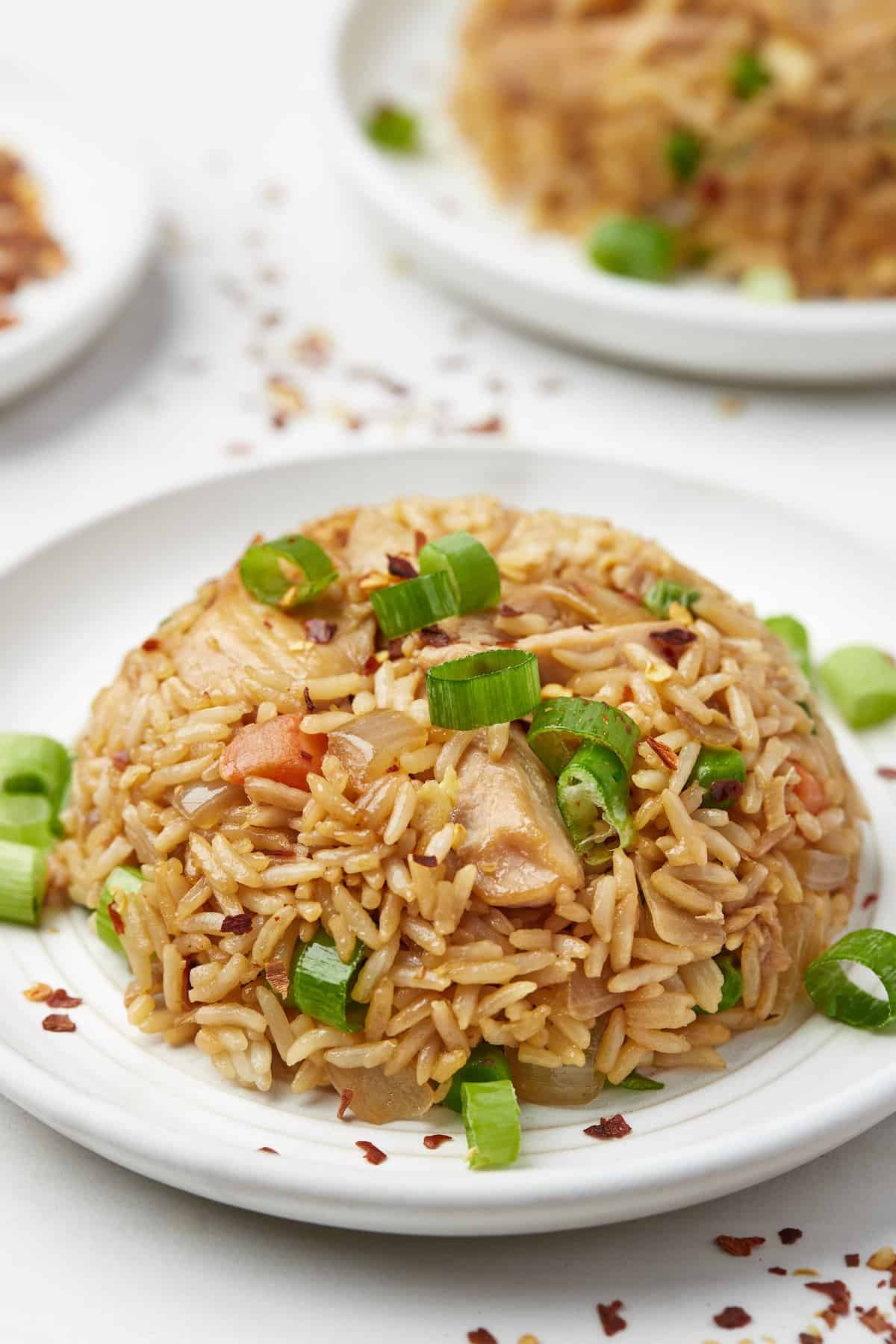 A pile of chicken fried rice on a small plate with chopped green onions on top as a garnish.