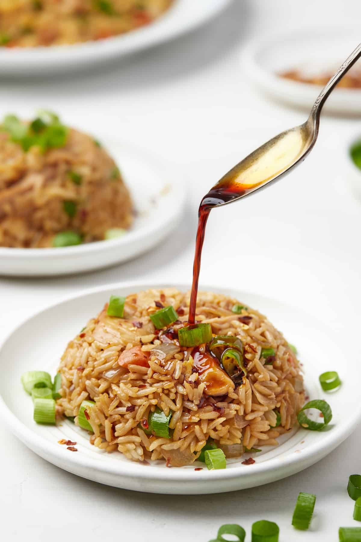 Extra soy sauce being spooned over a pile of fried rice on a small plate.