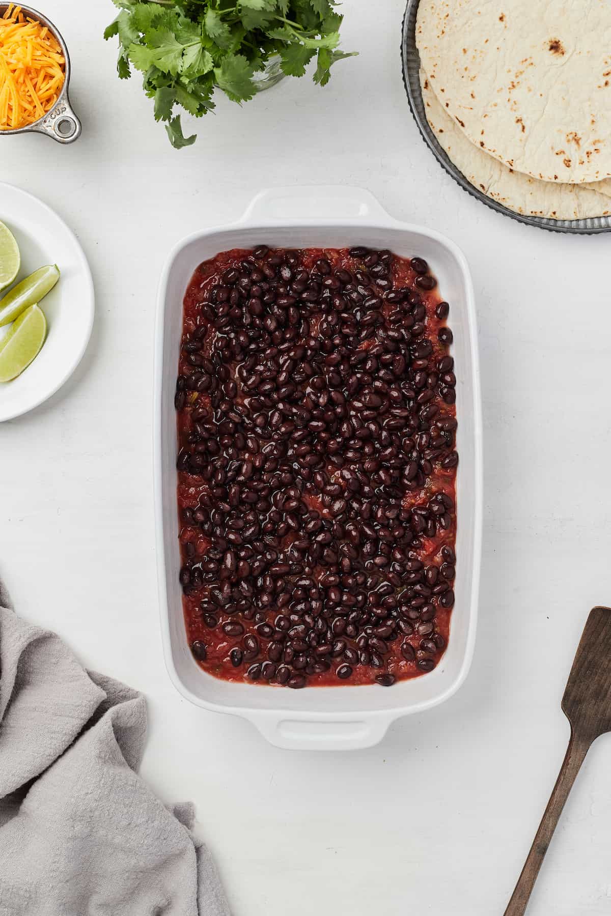 Salsa and black beans spread evenly into a white baking dish