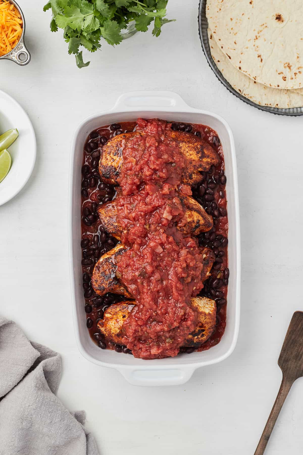 Salsa, beans and chicken layered into a baking dish with more salsa on top of the chicken