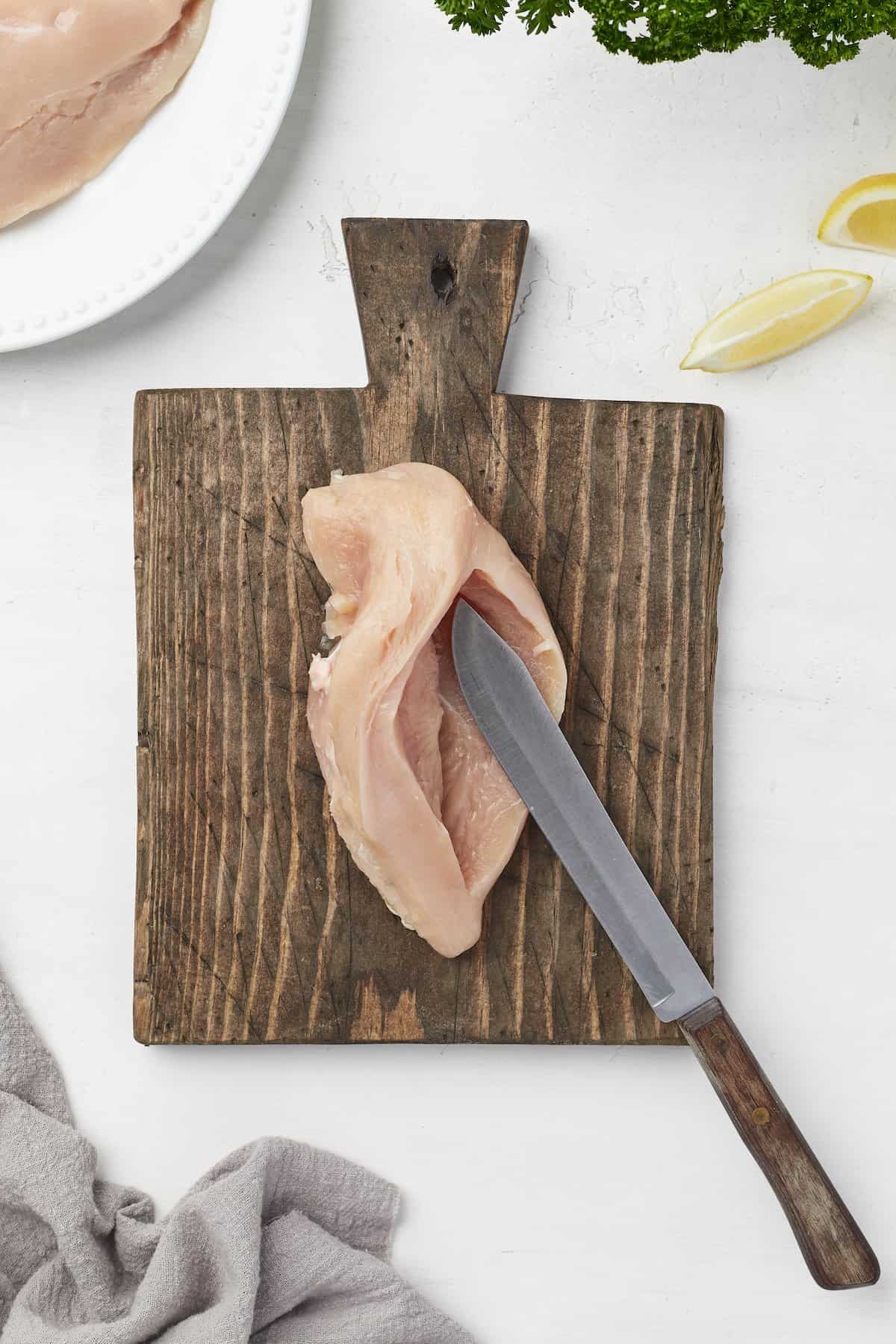 A boneless chicken breast with a slit cut into it on top of a cutting board with a knife