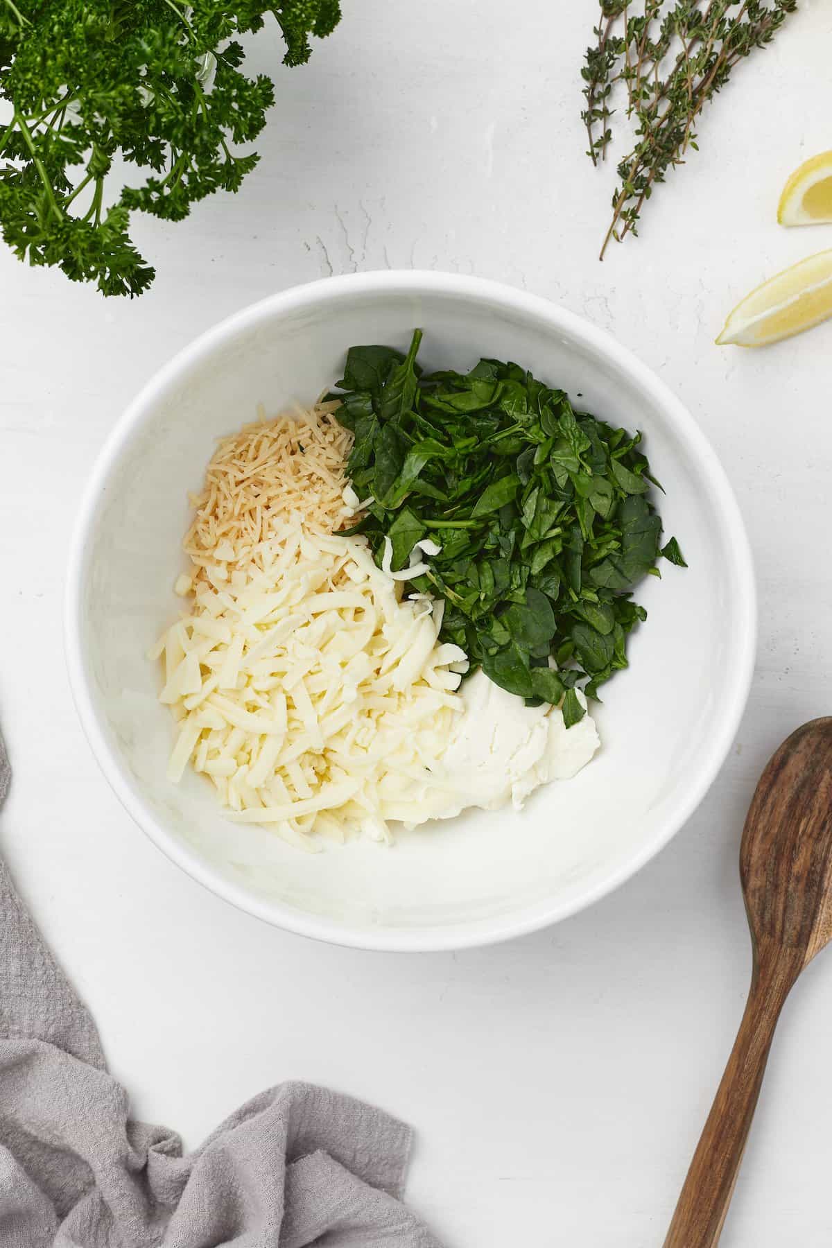 Spinach, parmesan cheese, mozzarella cheese and cream cheese inside of a mixing bowl
