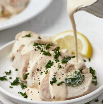 Slices of spinach stuffed chicken on a plate with cream cheese sauce being poured on top of the chicken