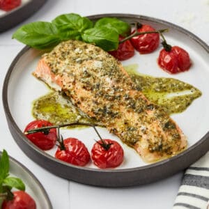 A plate of baked pesto salmon with roasted cherry tomatoes.