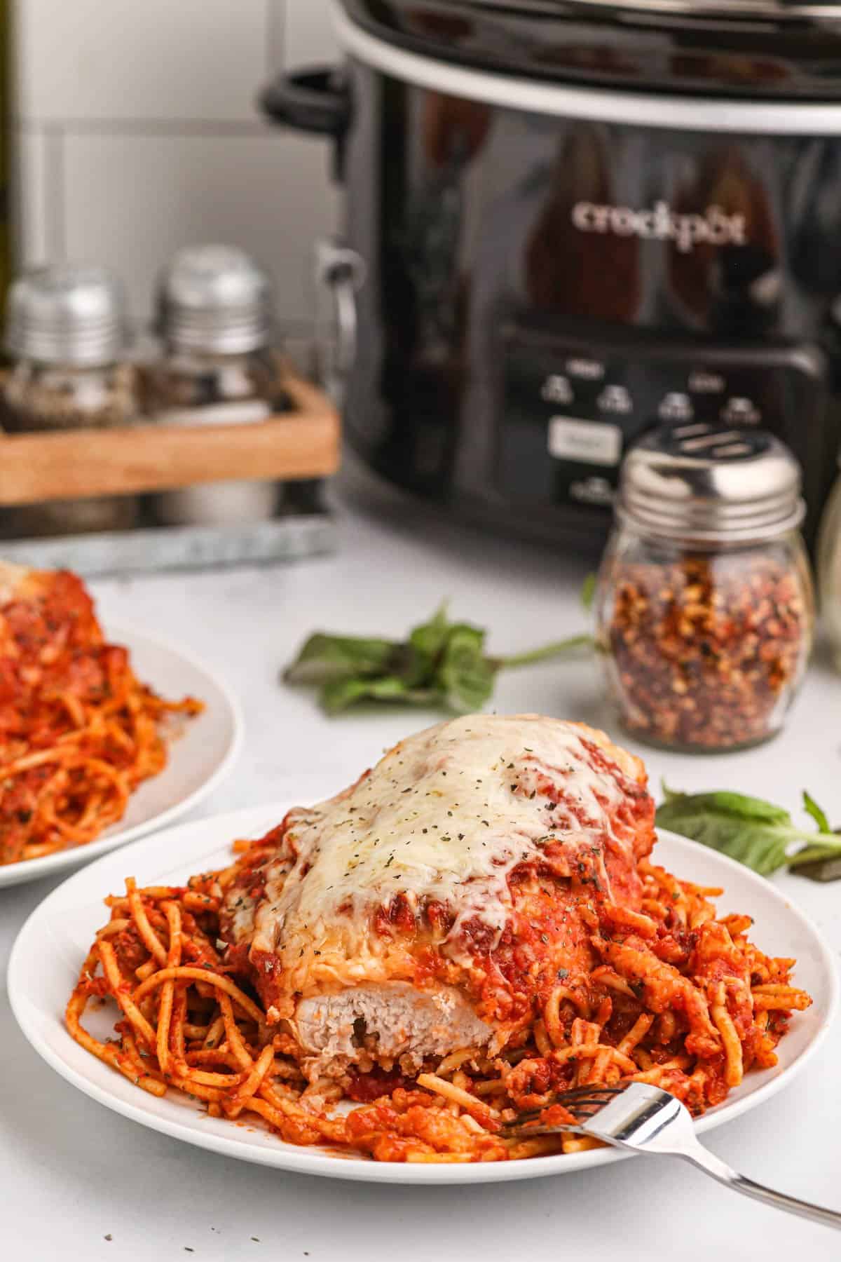 Chicken Parmesan made in the slow cooker on a plate in front of spices and a crock pot.