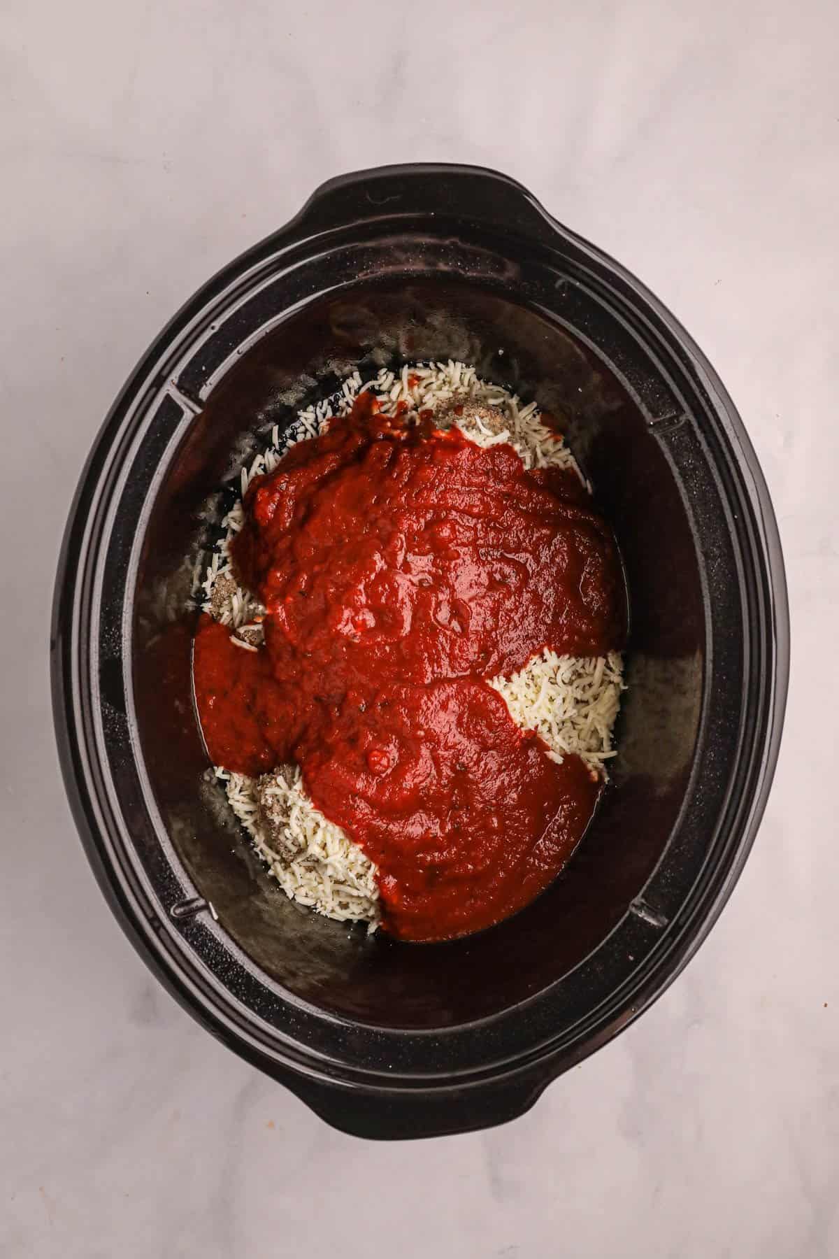 Adding marinara sauce on top of chicken and cheese in the slow cooker.