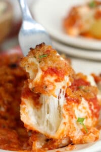 A fork lifting a bite of Olive Garden stuffed shells with stretchy cheese.