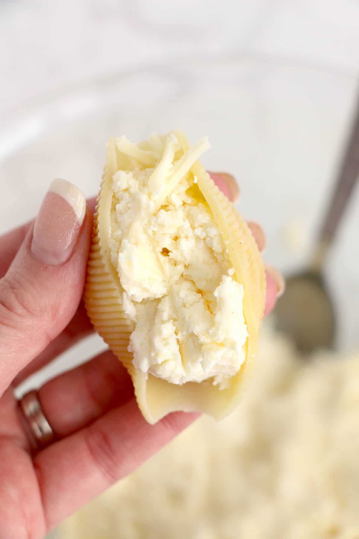 A hand holding a jumbo pasta shell filled with ricotta cheese mixture.