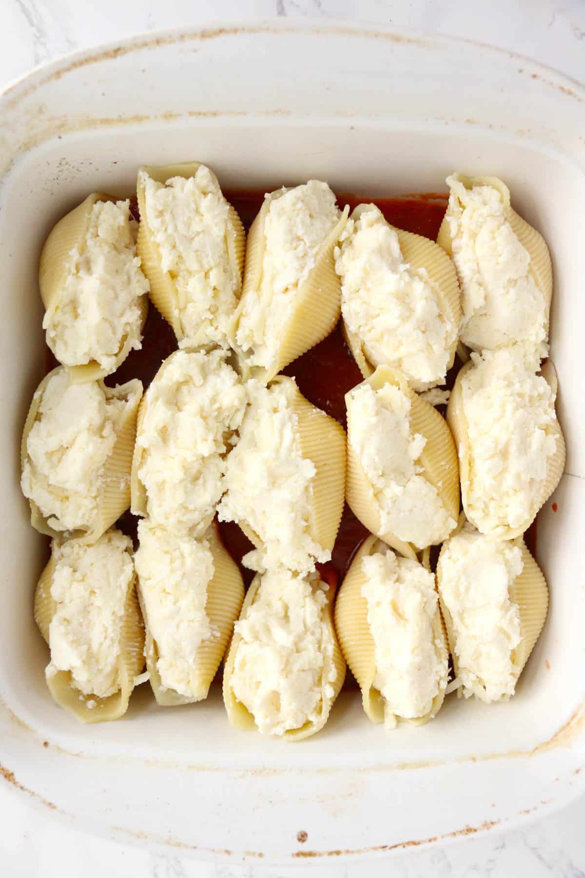 Jumbo pasta shells stuffed with cheese mixture in a white baking dish.