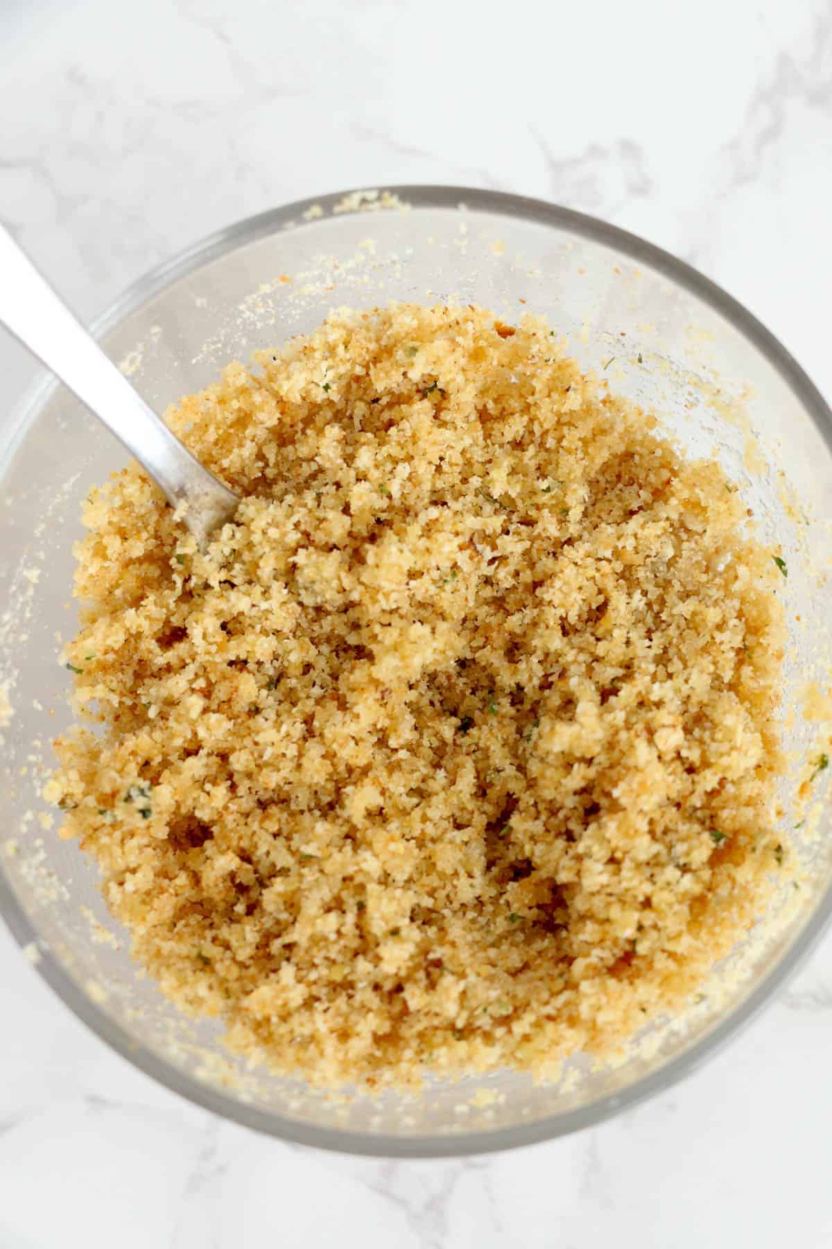 Stirring buttery seasoned breadcrumbs in a large bowl.
