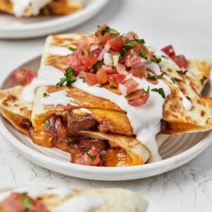 Plate of steak quesadillas stacked and topped with sour cream and pico de gallo.