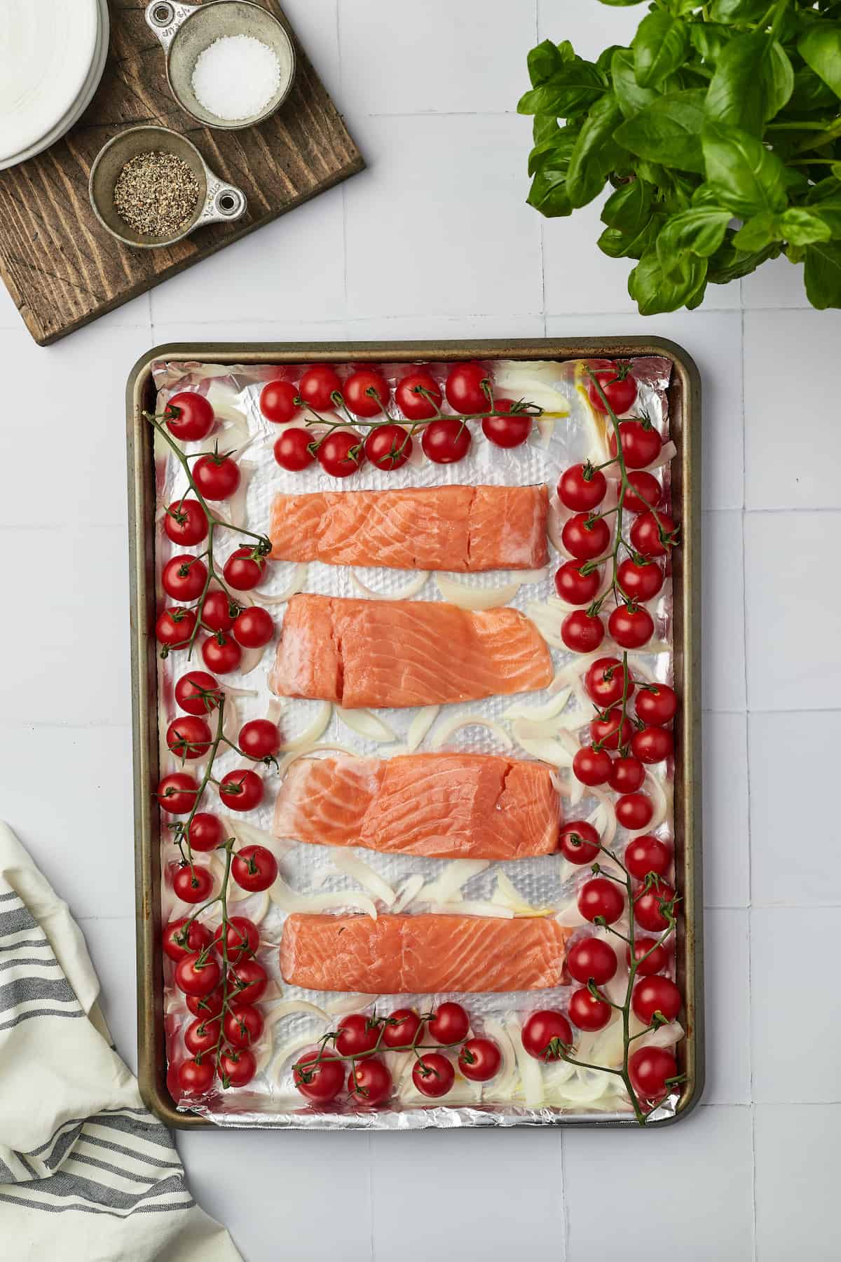 Overhead view of salmon fillets arranged on pan with cherry tomatoes