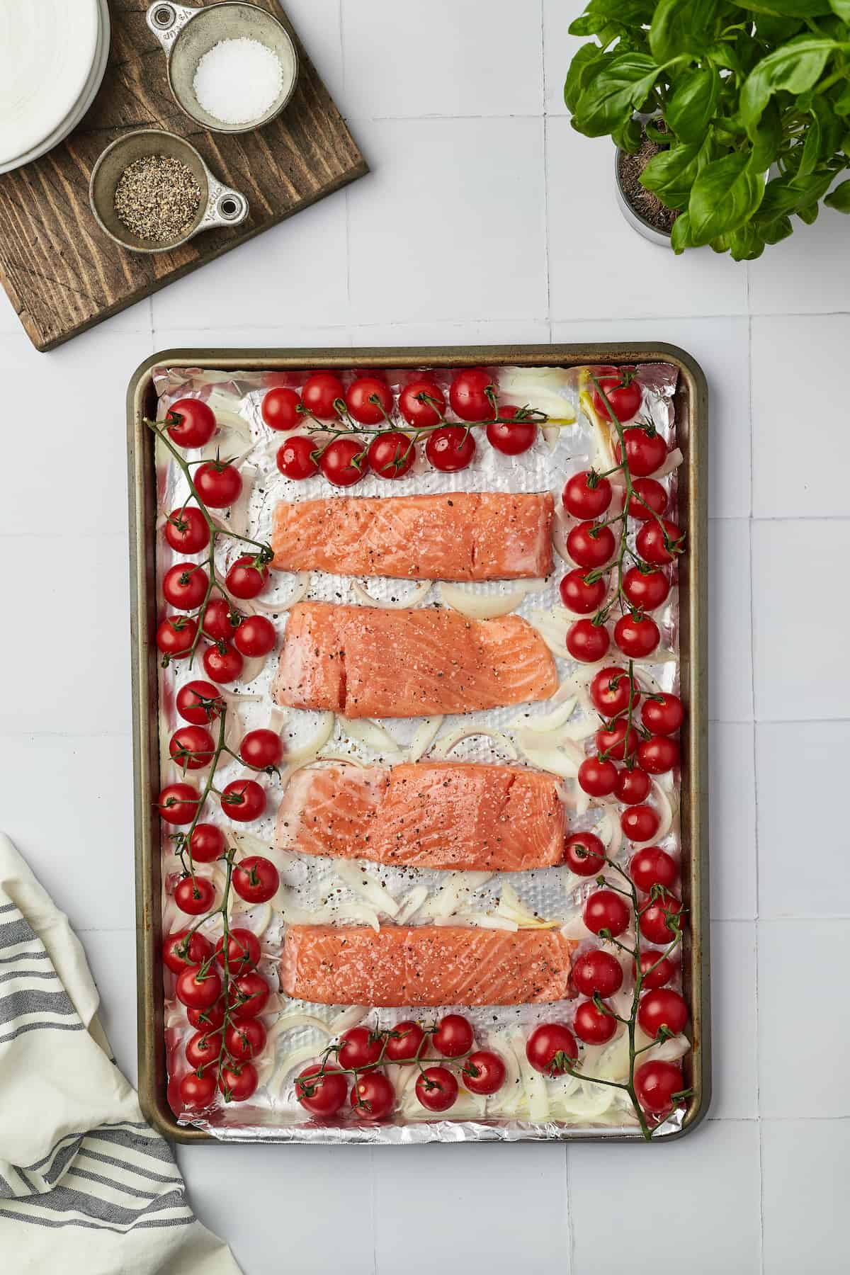 Overhead view of seasoned salmon fillets arranged on pan with cherry tomatoes