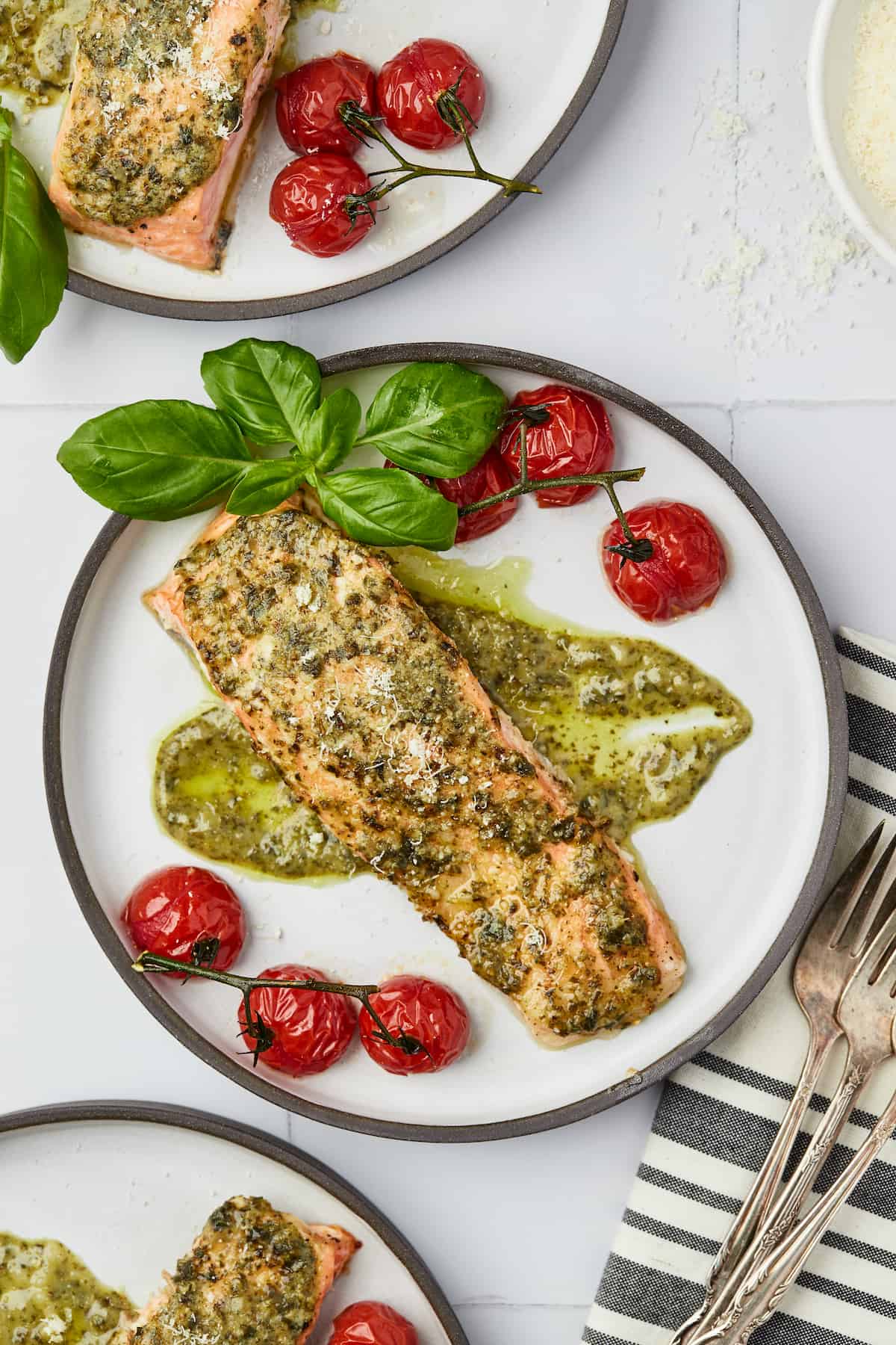Overhead view of baked pesto salmon on plate with basil and roasted cherry tomatoes