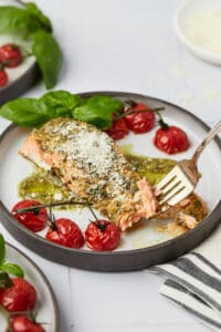 Baked pesto salmon on plate with roasted tomatoes and basil