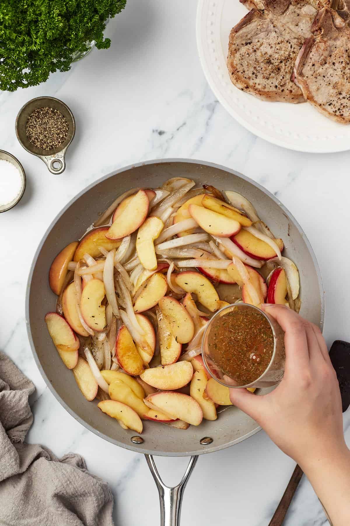 Pouring apple cider sauce into skillet with apples and onions