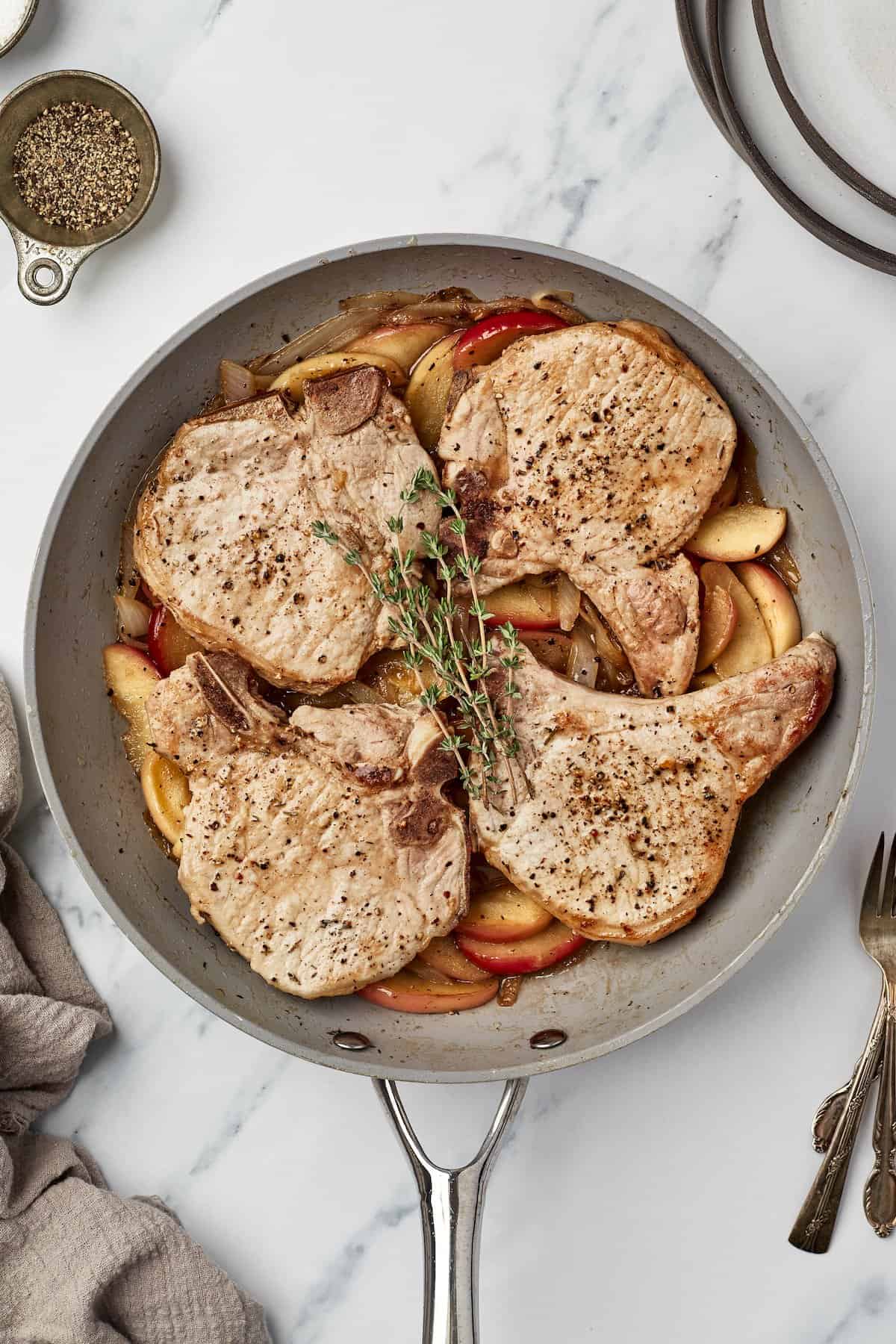 Overhead view of pork chops with apples and onions in skillet