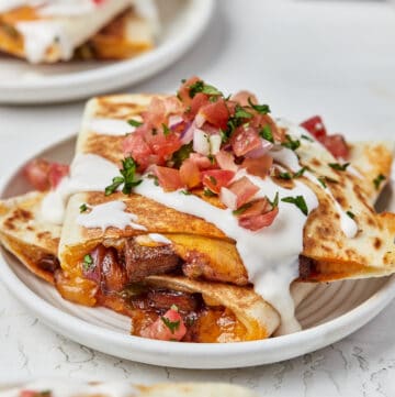 Plate of steak quesadillas stacked and topped with sour cream and pico de gallo