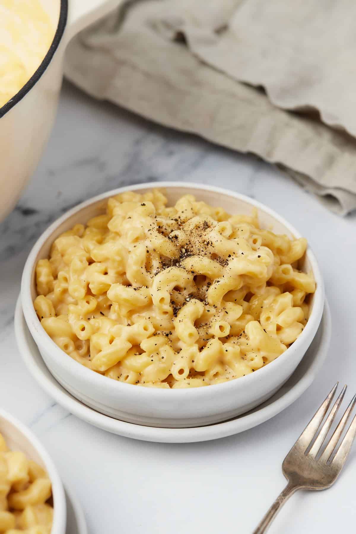 Stovetop mac and cheese in white bowl, seasoned with cracked black pepper