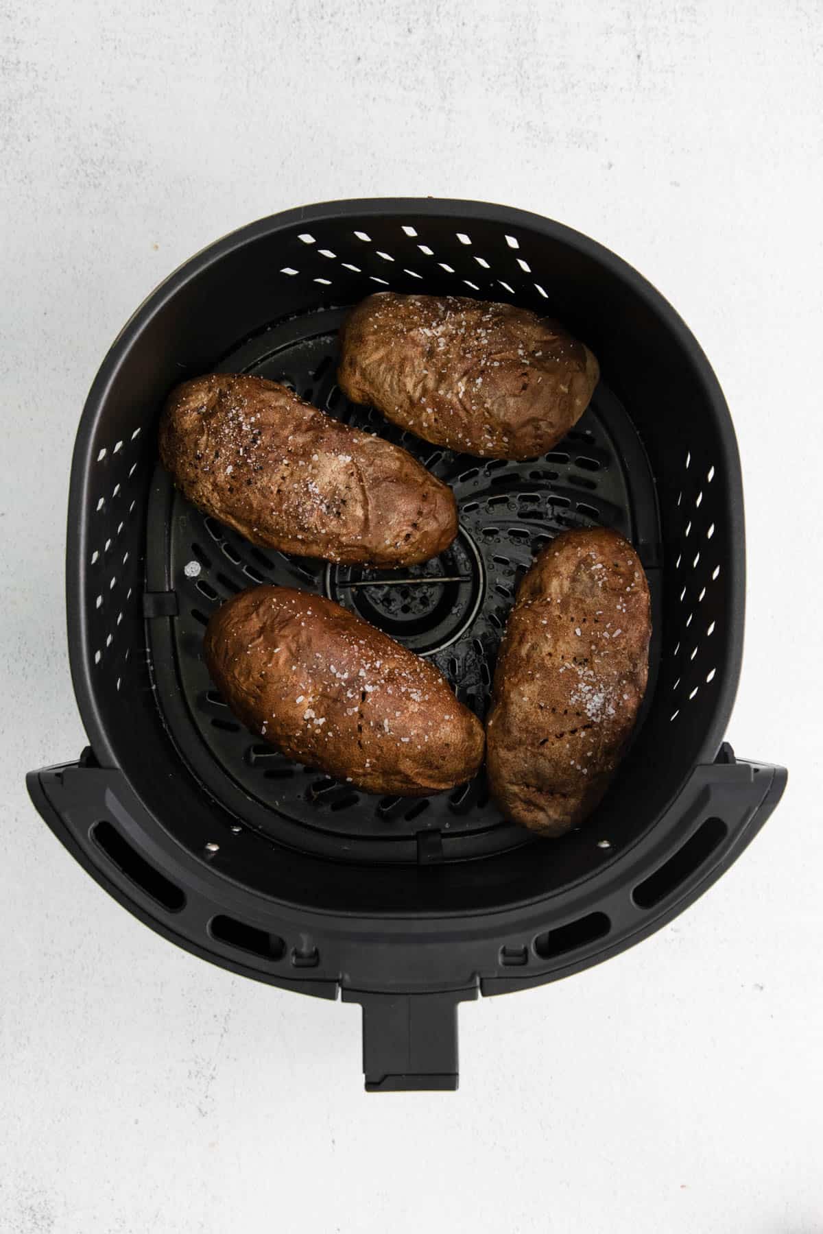 Four baked potatoes in the air fryer after being baked.