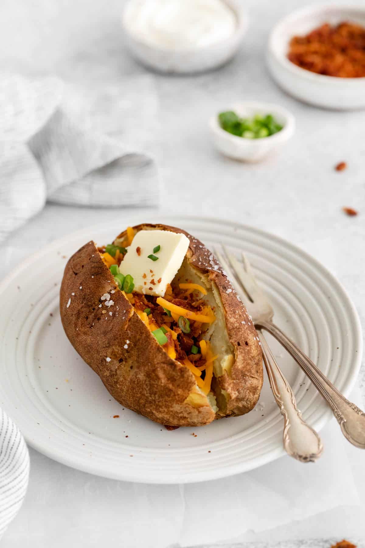 A baked potato with butter, cheese, and bacon on a white plate.