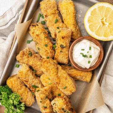 Tray of air fryer fish sticks with small bowl of tartar sauce and lemon half