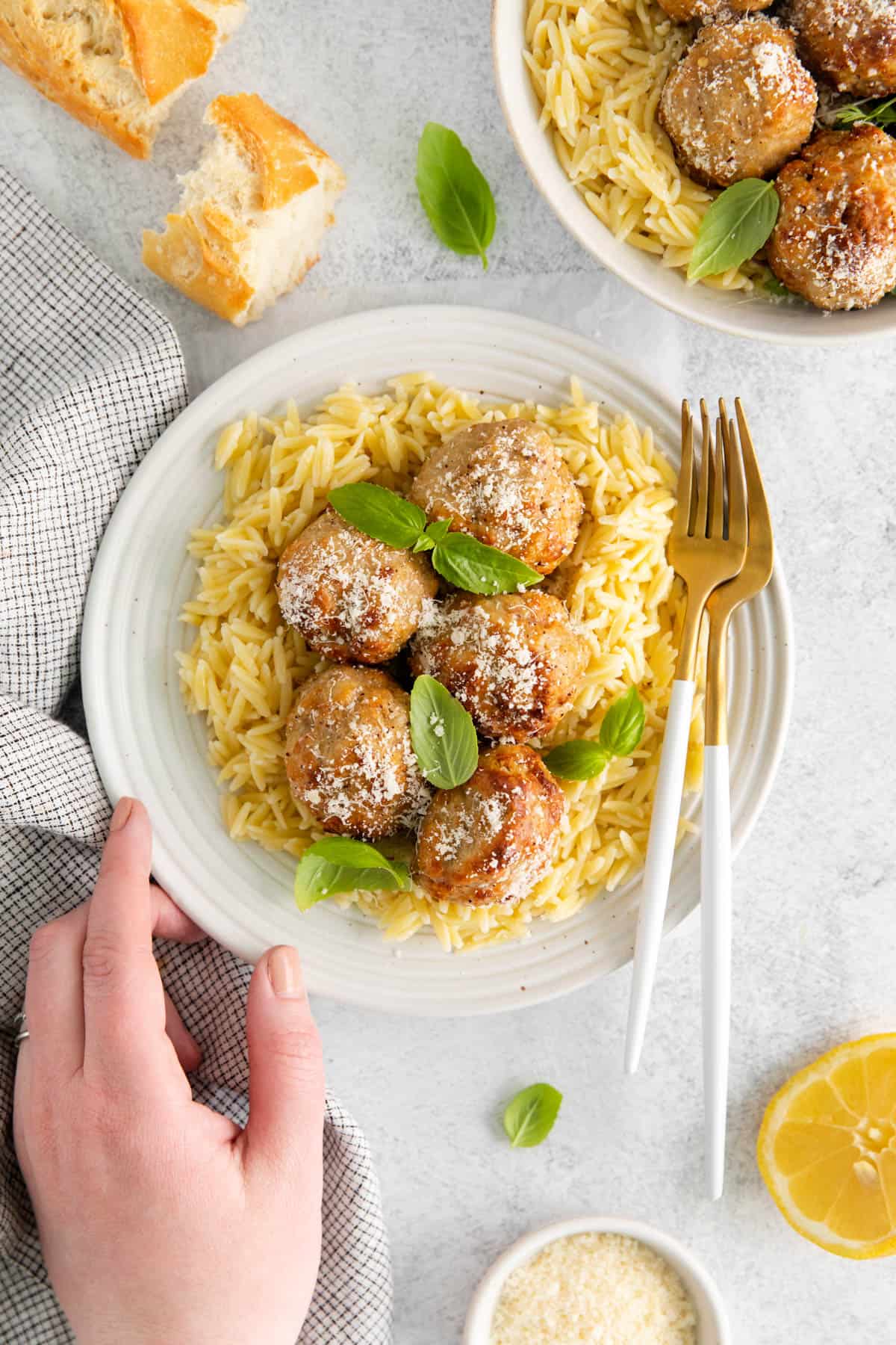 A hand reaching for a plate of lemon chicken meatballs.