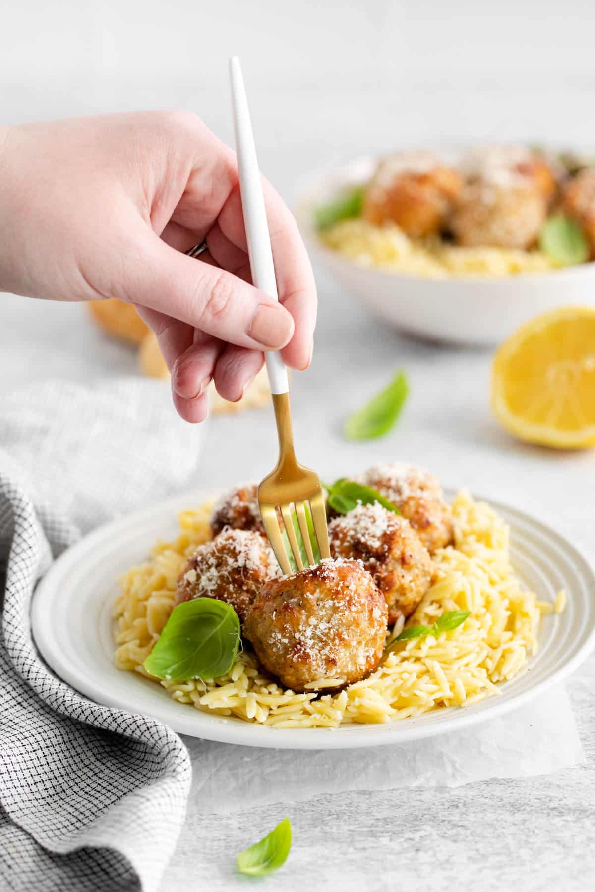 A fork spearing a lemon chicken meatball on a plate.