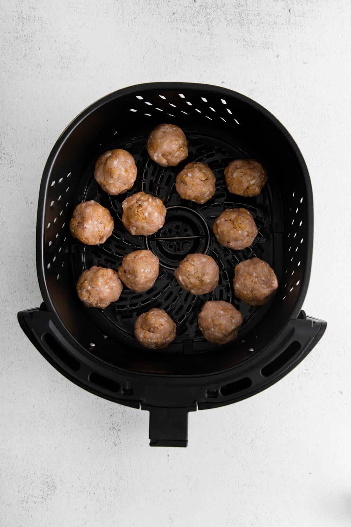 Uncooked chicken meatballs in an air fryer basket.