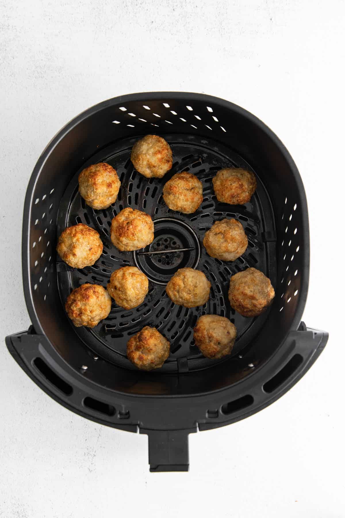 Partially cooked chicken meatballs in an air fryer basket.