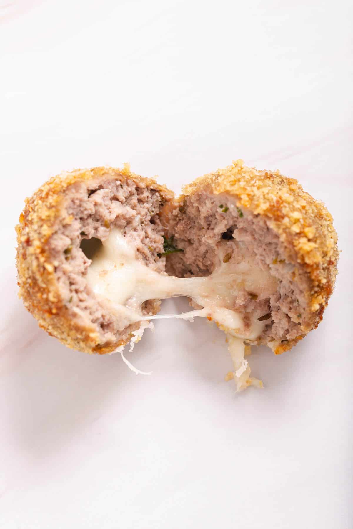 A cheese-stuffed meatball cut in half with cheese oozing out.