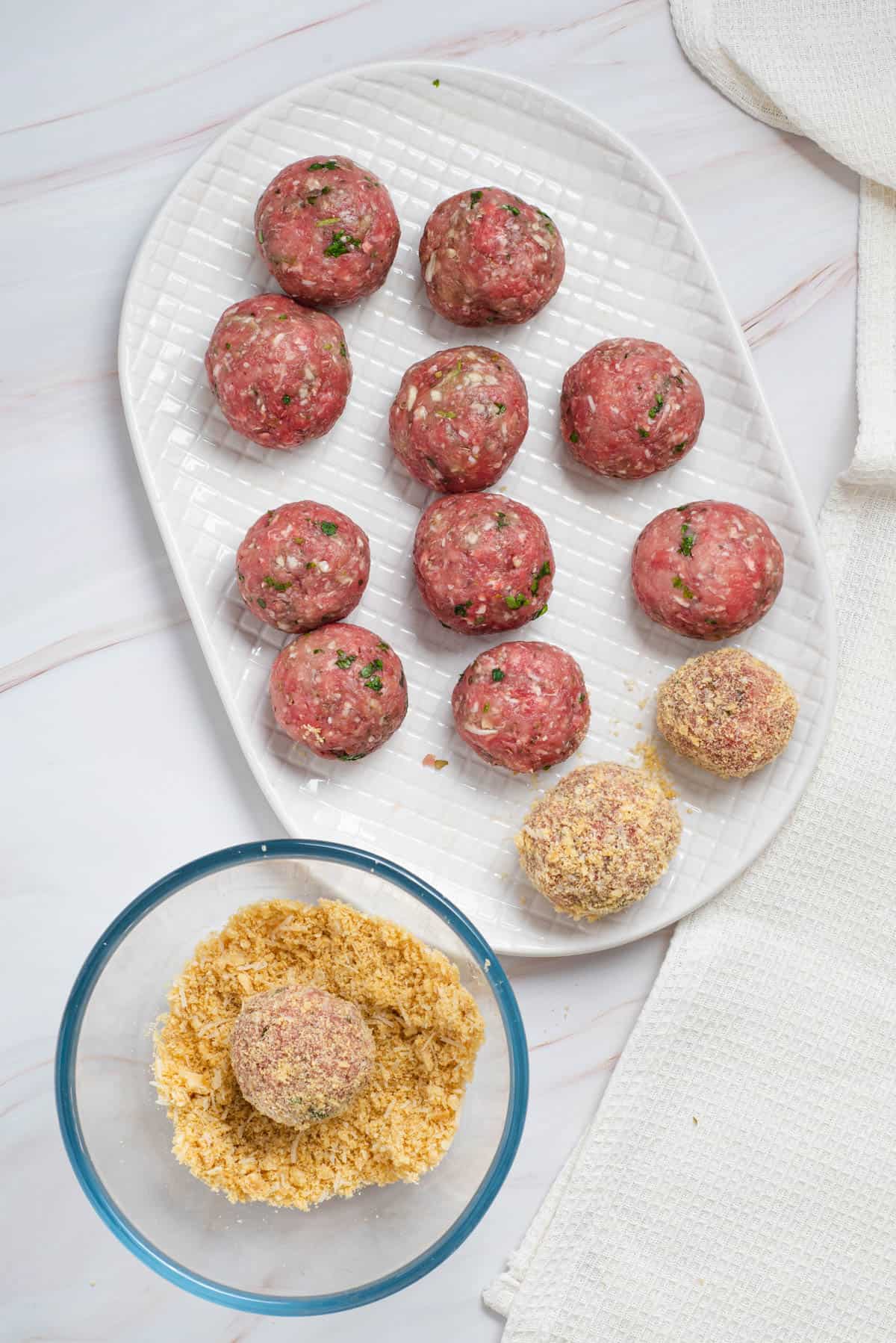 Coating cheese stuffed meatballs in seasoned breadcrumbs.